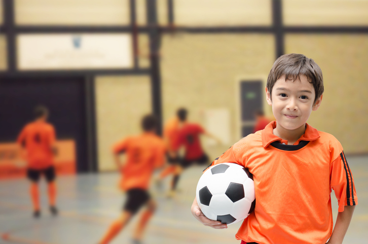 Boy holding a soccer ball in a gymnasium.